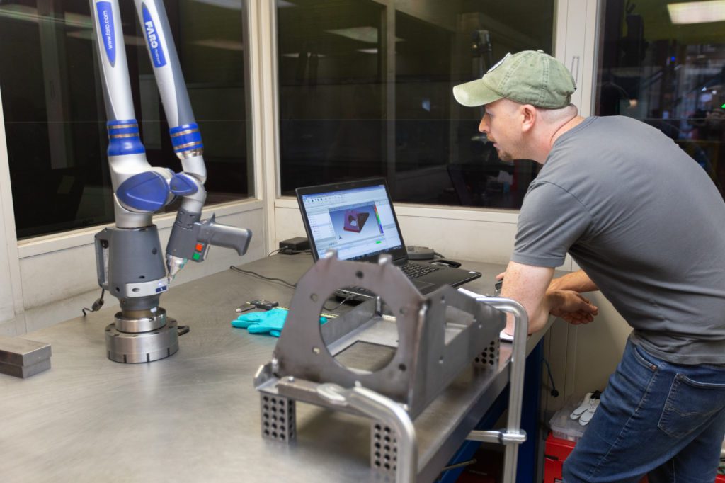 man stands at desk with a laptop testing a metal work product