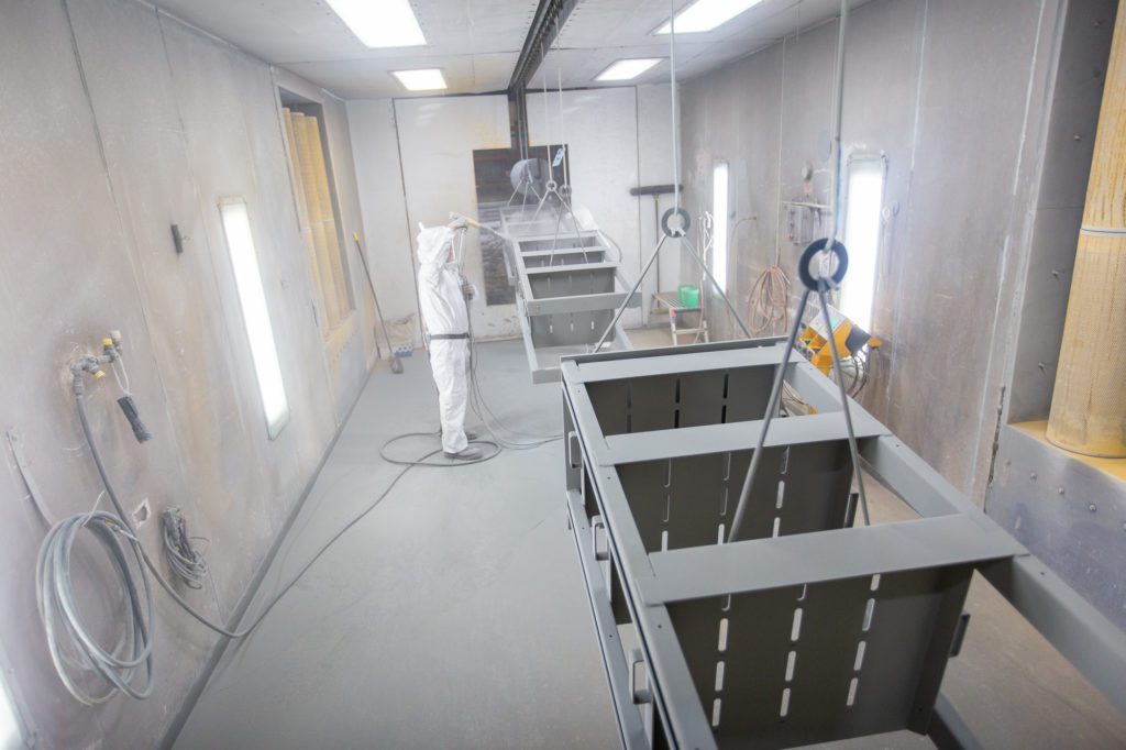 man wearing protective gear completing batch powder coating on multiple metal parts