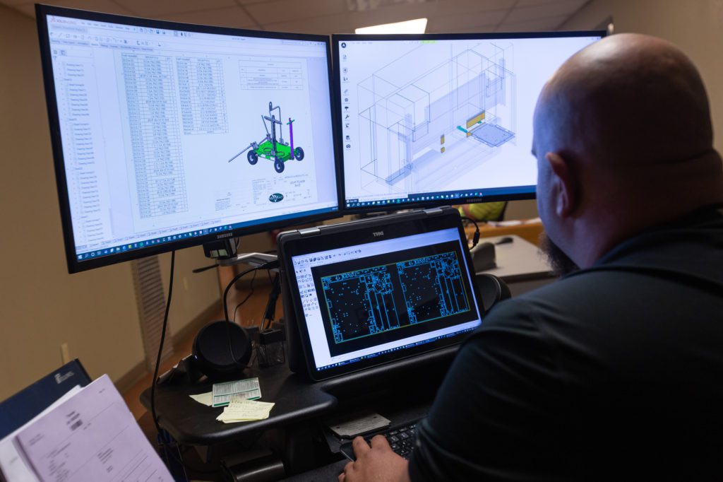 man working on laptop and computer screens on metal design work